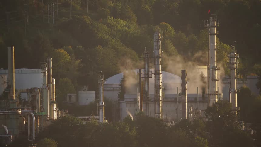A refinery plant with steam rising from several chimneys at midday
