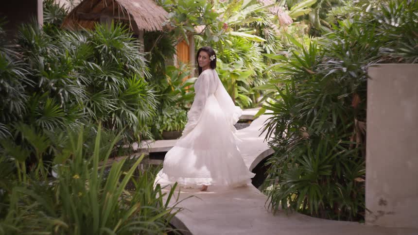 A young lady running on a path with plants lining both sides of the wall during a vacation at midday