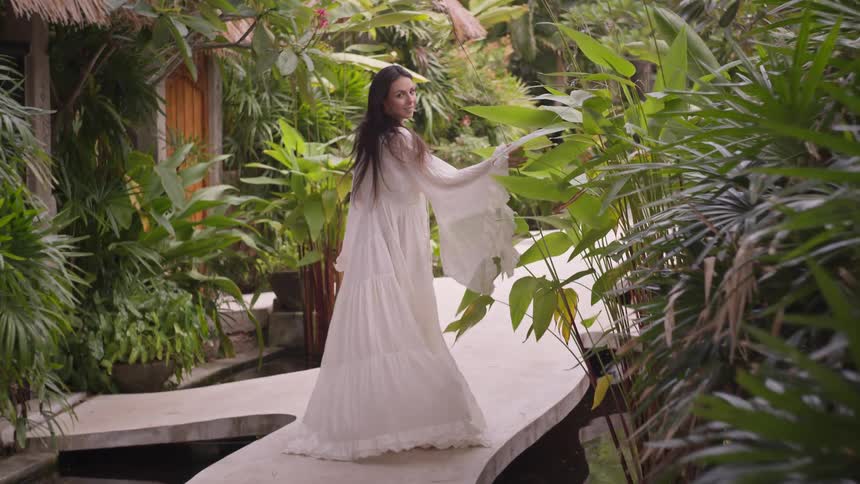 Woman in a long white dress walking along a walkway surrounded by tropical plants
