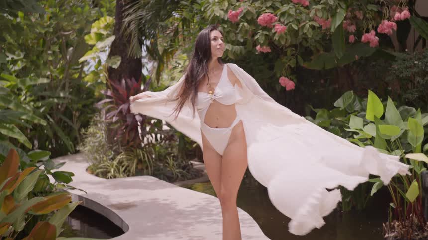 Woman smiles while twirling in a white coverup in a tropical garden