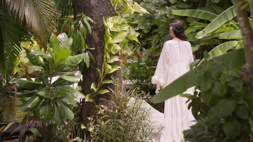 Woman walking through a tropical garden wearing a long white dress