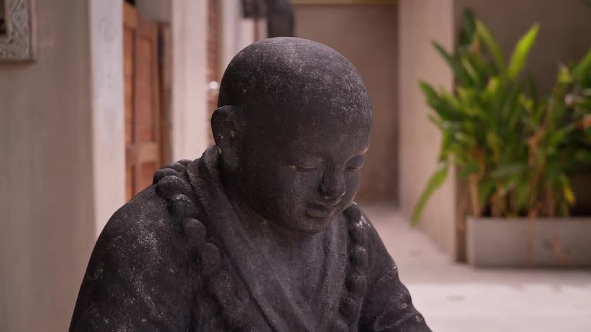 Stone statue of a monk with prayer beads in an outdoor setting