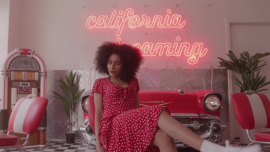 Woman in a red polkadot dress posing by a vintage car in a retro diner