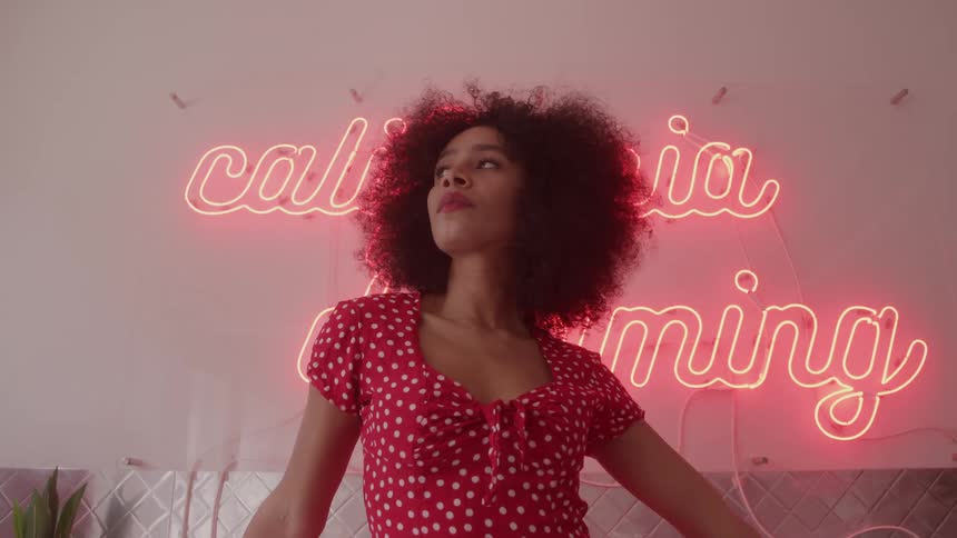 Woman in a red polka dot dress in front of a pink neon sign