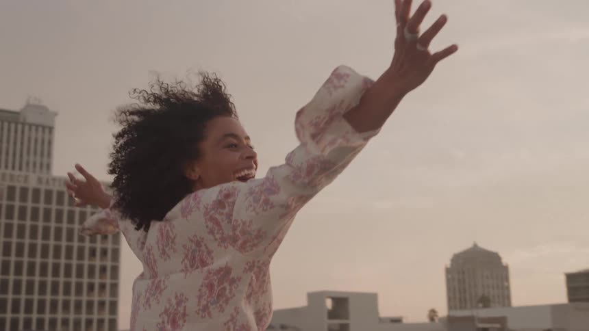 A woman joyfully raises her arms with city buildings in the background