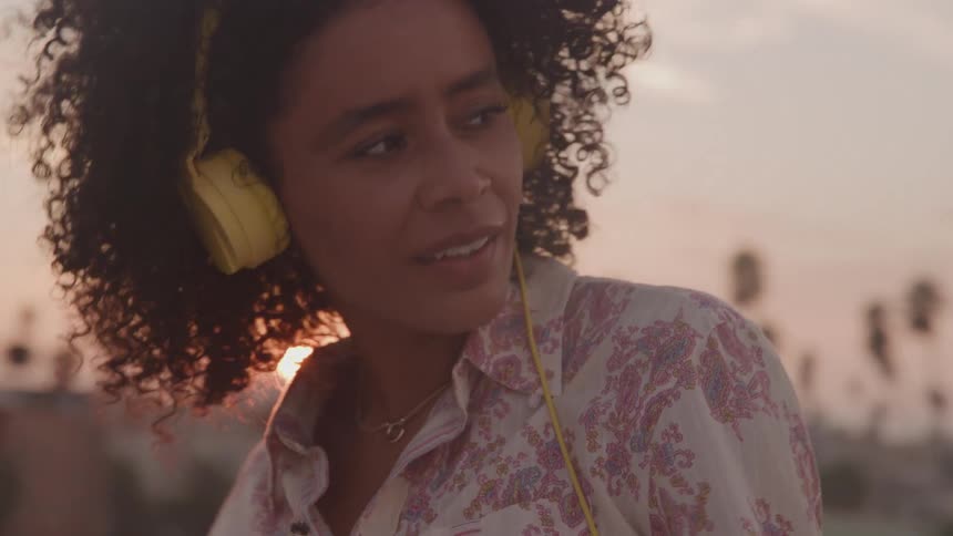 A woman wearing headphones dances outdoors while listening to music