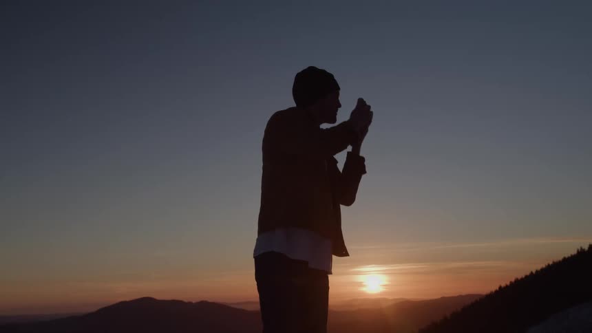 The man is taking photos of the mountains at sunset
