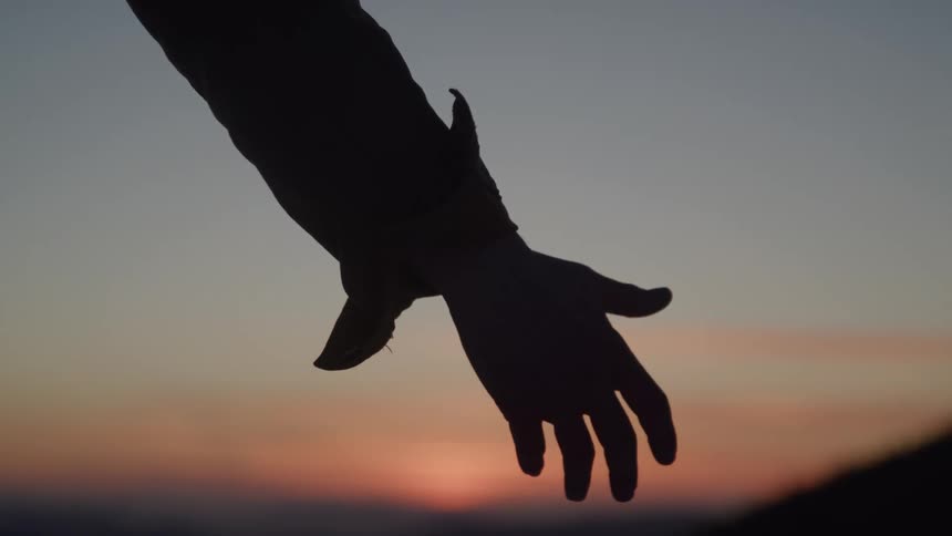 The person reaches out their hand as the sun sets