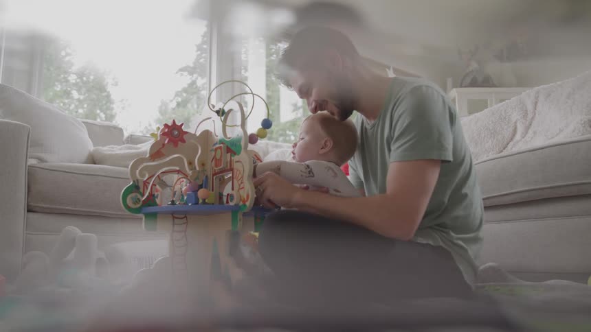 A man and a baby are sitting on the floor playing with a wooden activity toy the room is filled with natural light