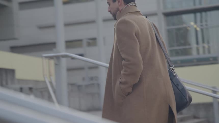 Man in a long brown coat walking up an outside staircase