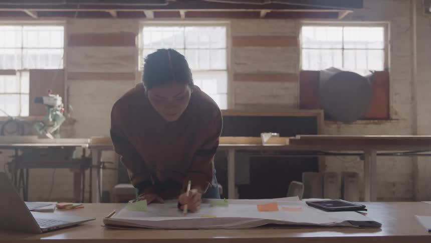 A woman draws a design at a wooden desk in a workshop