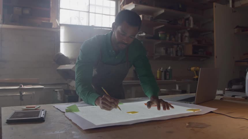 The worker is using a pencil to sketch on the blueprints