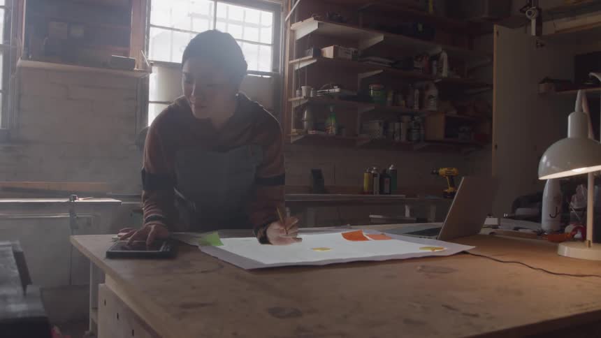 The woman is writing and using a tablet on the workbench