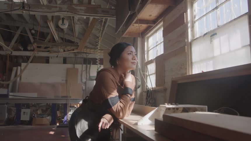 A woman looking thoughtfully out of a window in a workshop