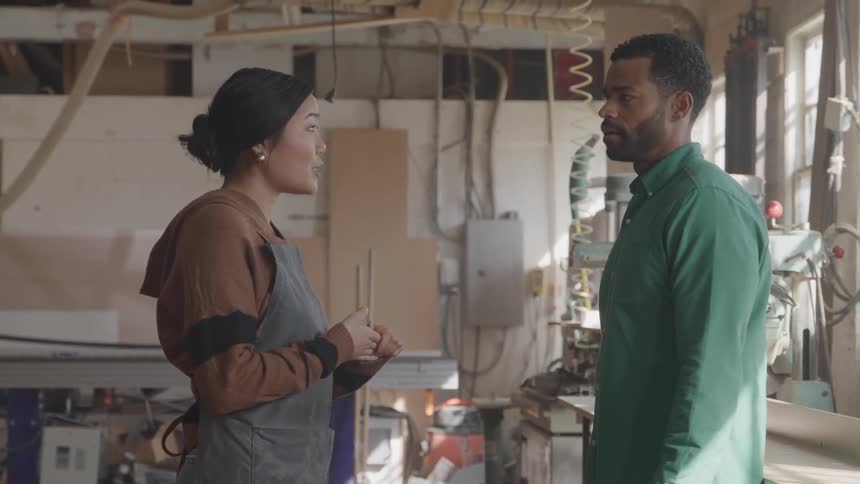 Smiling woman talking to a man in a workshop both wearing work clothes