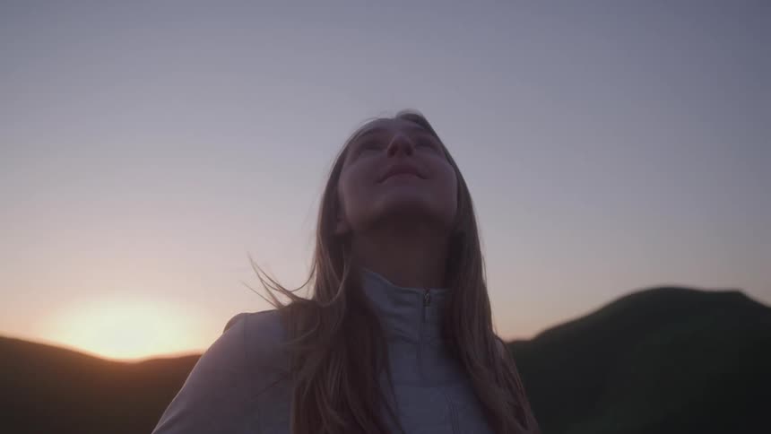 A young woman stands outdoors and looks up at the sky
