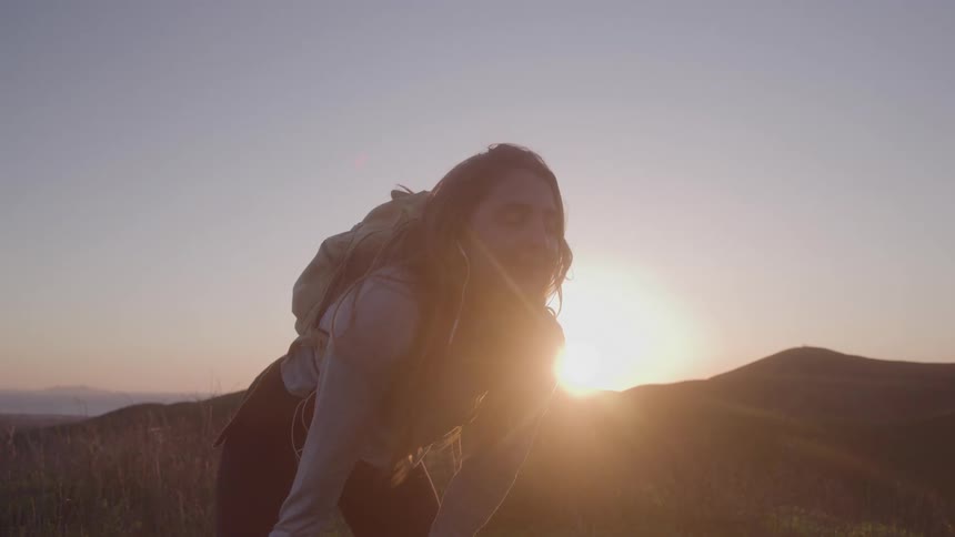 Person with a backpack during an outdoor hike lit by the setting sun behind the hills