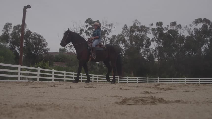 Woman with a hat riding a horse inside an enclosure