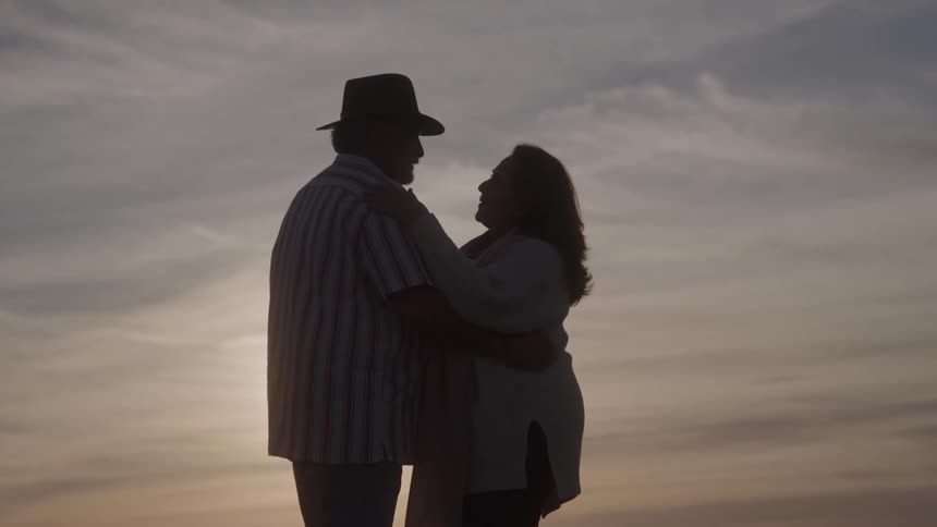 A couple is silhouetted against a cloudy sky during sunset they are standing close together and appear to be embracing