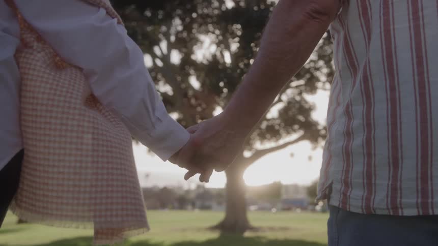 Two people walk away from the camera while holding hands