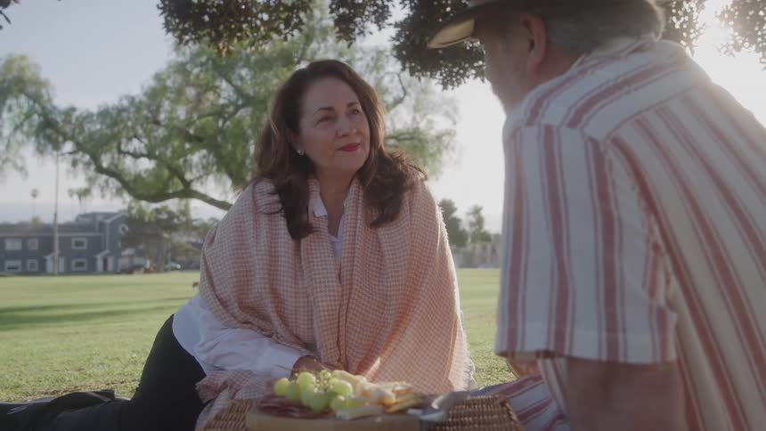 Close up of a middle aged couple sitting together on a field outdoors for a romantic picnic during daytime