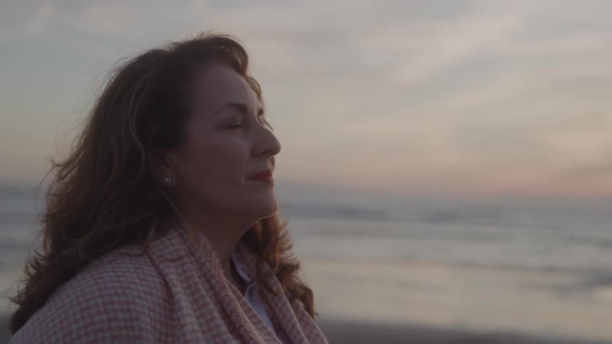 Woman with closed eyes enjoying the sea breeze at dusk