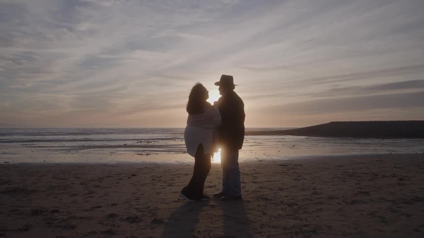 Couple facing each other close standing at the beach at sunset