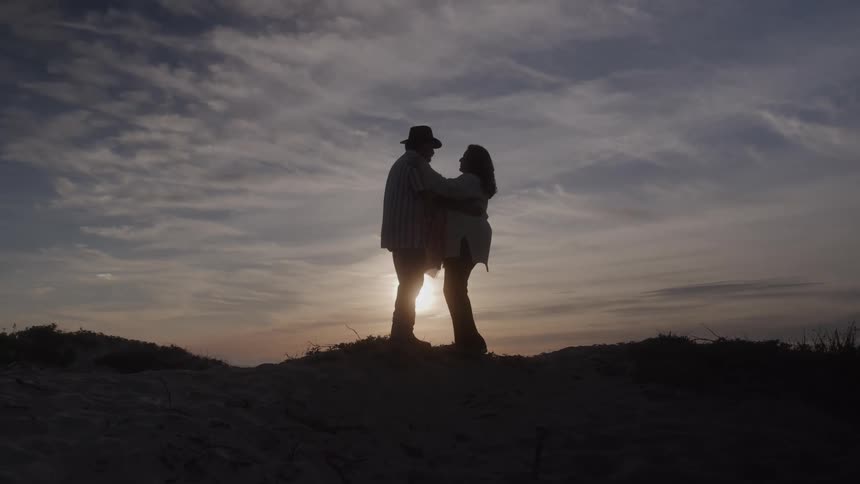 Couple holding hands faces each other at sunset on the sand