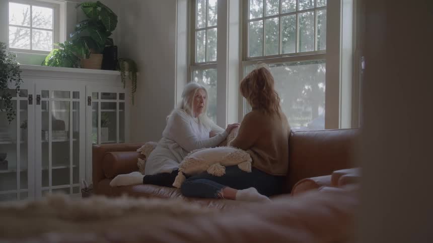 Elderly woman and young woman sitting on the couch talking in front of the windows