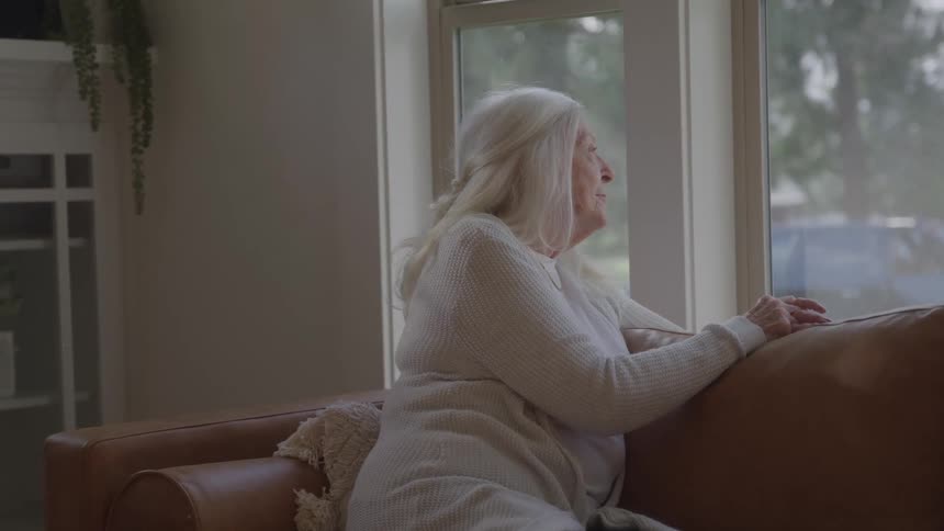 Elderly woman leaning on the couch looking out the window