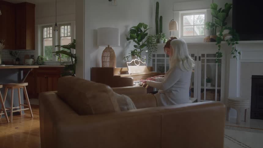 Mother and daughter playing a piano while sitting together in a living room during daytime
