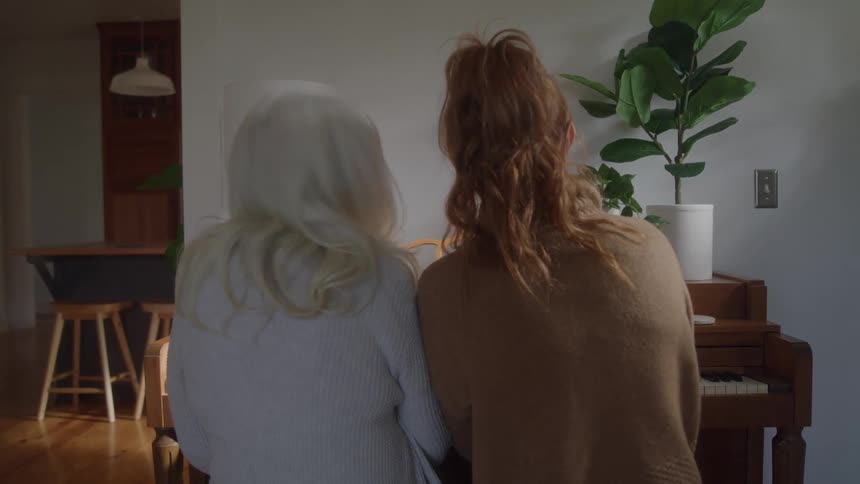 Elderly woman with white hair and young woman with a ponytail laugh together while sitting at the piano