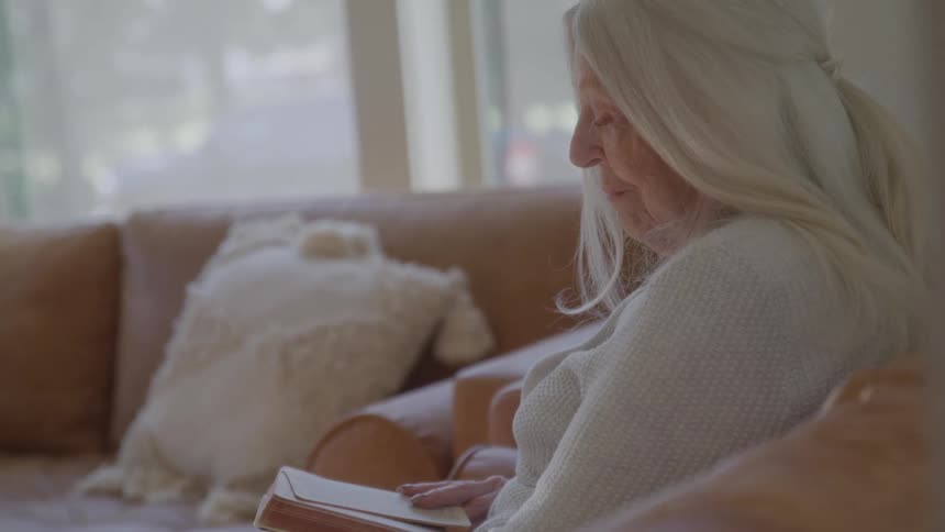 Elderly woman reading a book while sitting on the couch