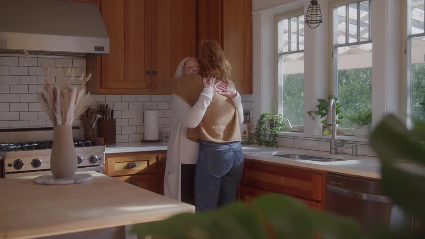 Two women hug in the kitchen lit by daylight