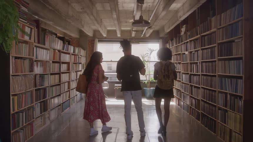 Three people walk through a hallway filled with bookshelves