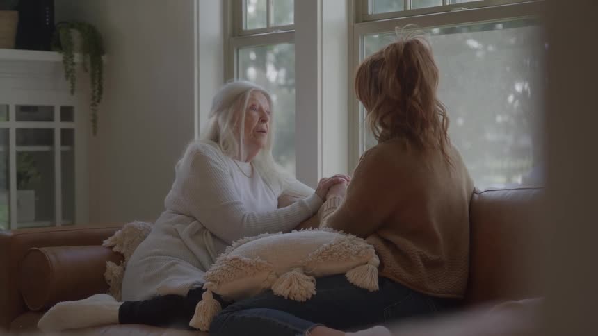 Elderly woman holding a young womans hands during a conversation on the couch
