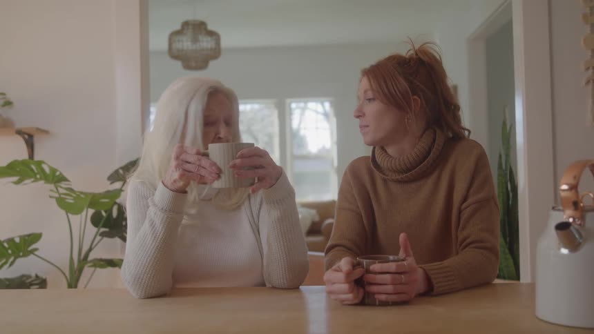 Two women talk while having coffee in a bright kitchen