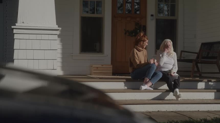 Two women talk while sitting on the steps of a porch