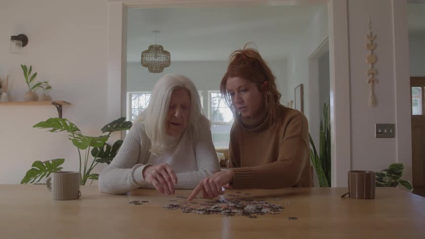 Collaborative puzzle assembly between elderly woman and adult woman in a modern residential setting