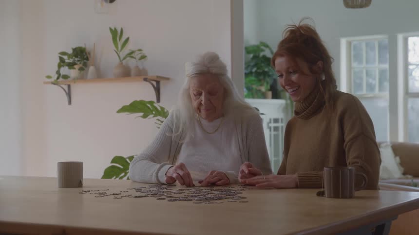 Two women happily solving a puzzle while sitting indoors