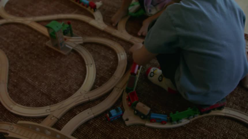 Child playing with wooden trains on a track set up on the carpet