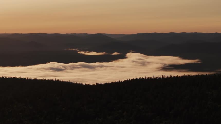Mountains at sunset surround a valley covered by low clouds