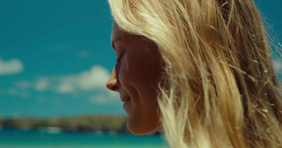 Profile of a blonde woman gazing at the horizon by the sea on a sunny day