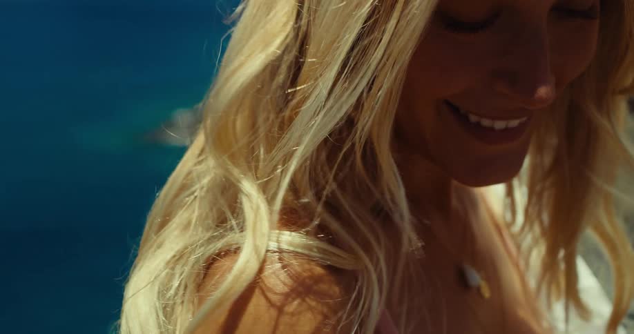 Blonde woman smiles in closeup as the wind blows her hair by the sea