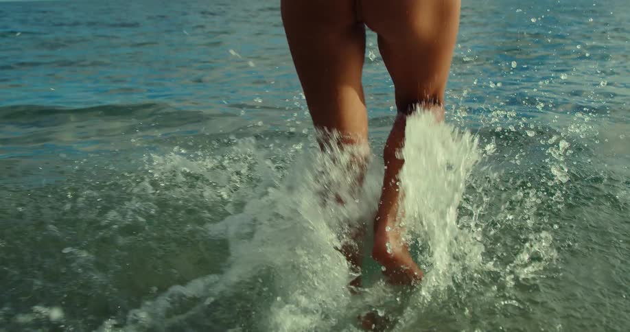 Woman runs through the sea with water splashing around her legs