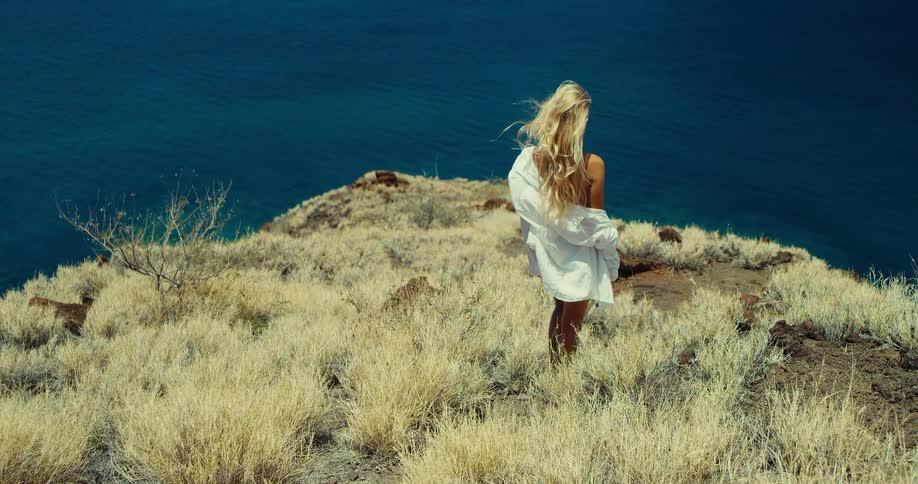 A person walks down a dry grassy hill toward a large body of water