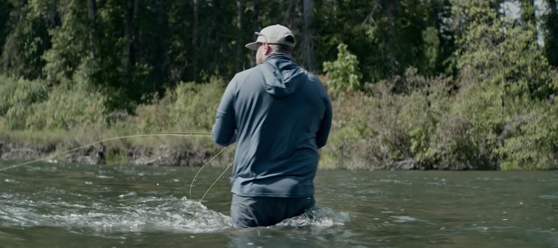 Man fishes in a shallow river surrounded by dense vegetation