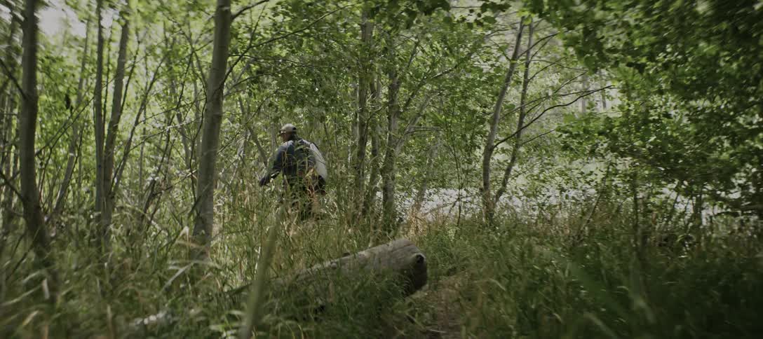 The man is heading towards the creek through the forest