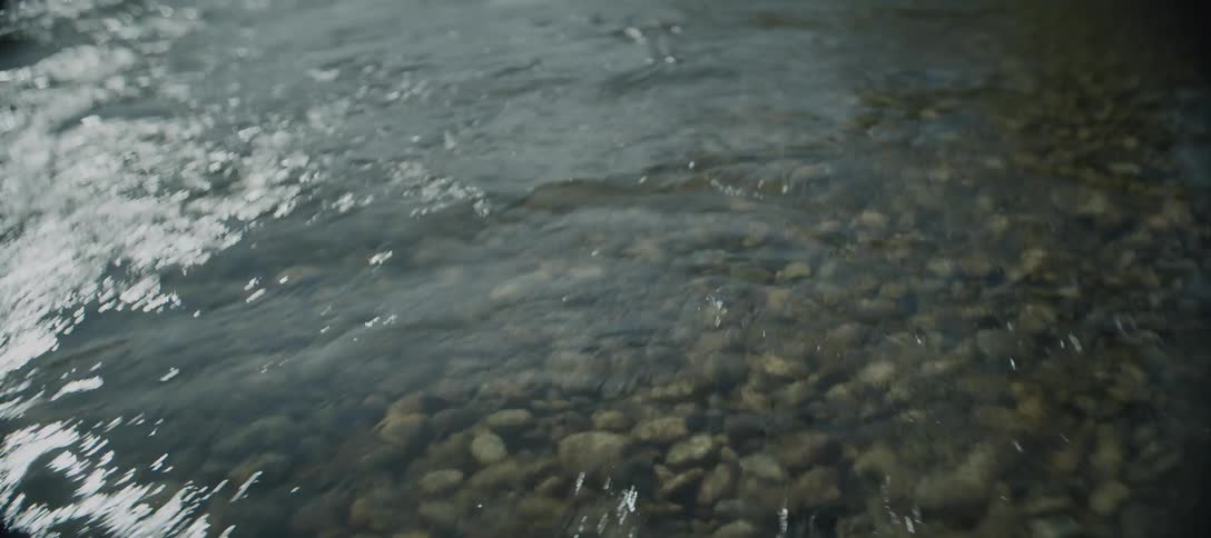 A shallow river water flows gently over smooth pebbles