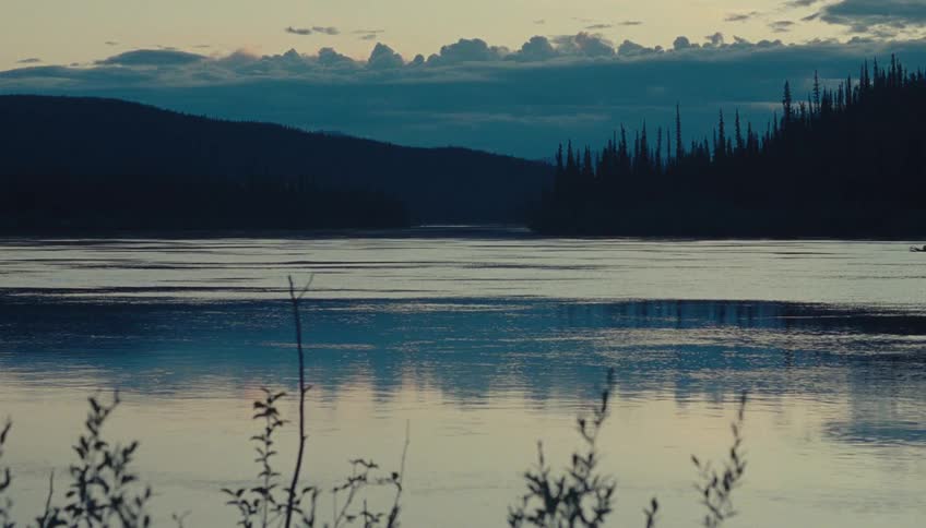 Evening reflection colors the calm river surface between hills